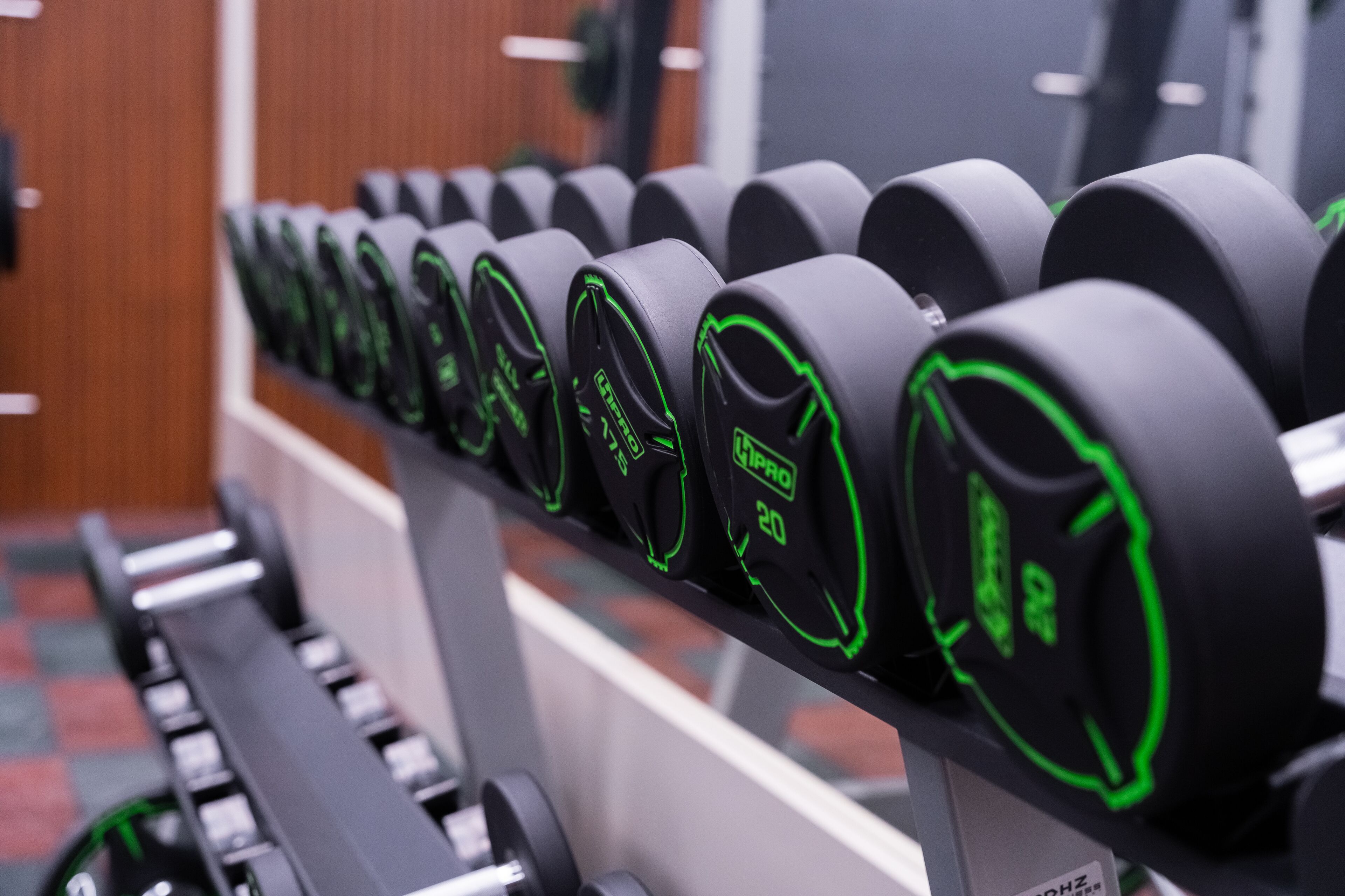 A row of black dumbbells with green accents, labeled with weight and model numbers, on a rack in a gym.