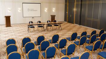 Una sala de conferencias con una larga mesa y sillas azules, una pantalla de proyector y un atril.