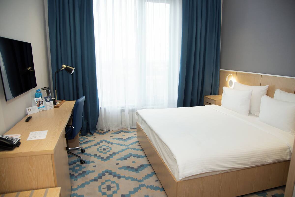 A hotel room with a bed, desk, chair, and a TV on the wall.
