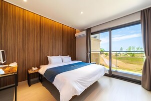 A modern hotel room with a large bed, a desk with a computer, and a view of the outdoors.