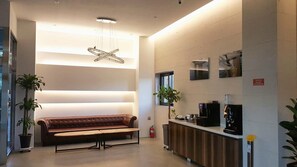 Eine moderne Lobby mit einer Lederbank, einer Kaffeestation und einer außergewöhnlichen Deckenleuchte.