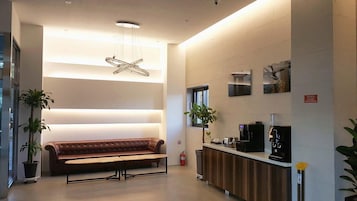 A modern lobby with a leather bench, a coffee station, and a unique ceiling light fixture.