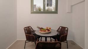 Un petit coin repas avec une table ronde, quatre chaises en osier, un panier de fruits et deux verres de jus d’orange.