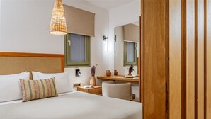 Hotellihuone, jossa on sänky, yöpöytä, tuoli, työpöytä, peili ja riippuvalaisin.
