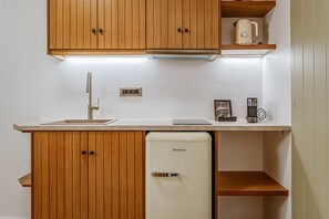 A compact kitchen with wooden cabinets, a white refrigerator, a sink, and a coffee maker.