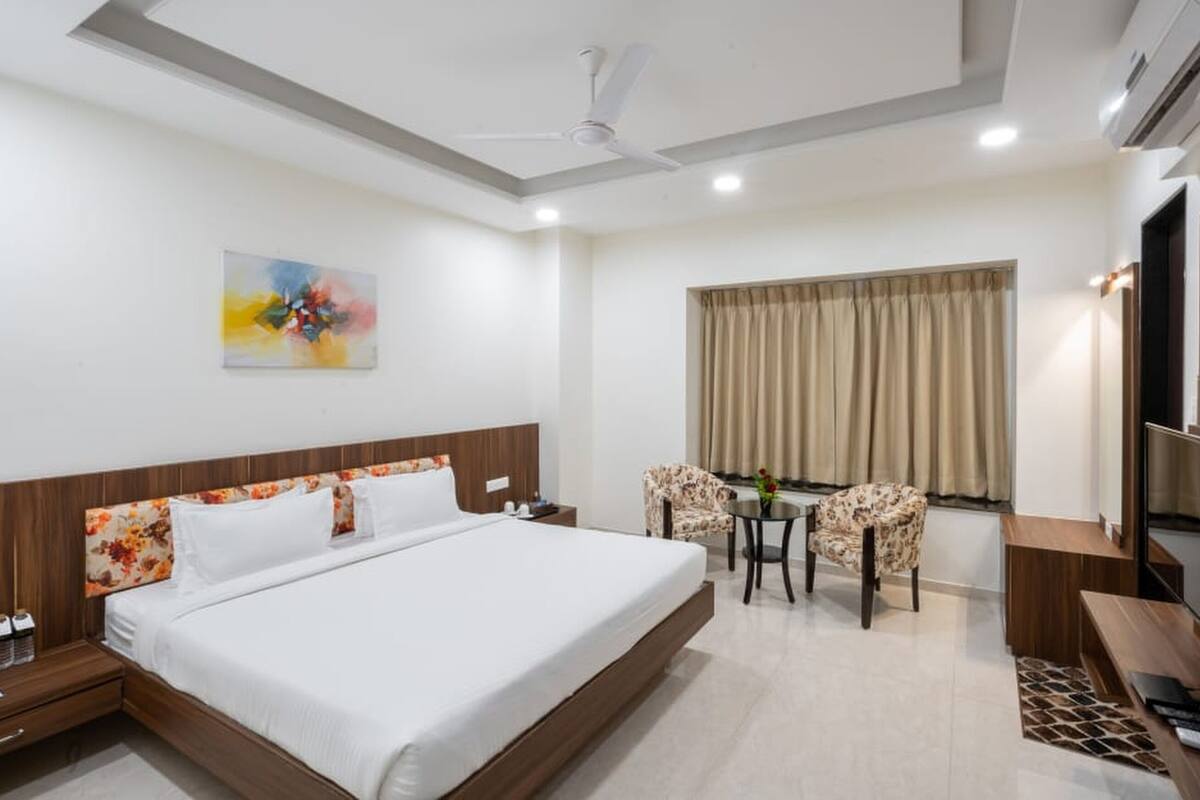 A hotel room with a large bed, a desk with a chair, a TV, and a ceiling fan.