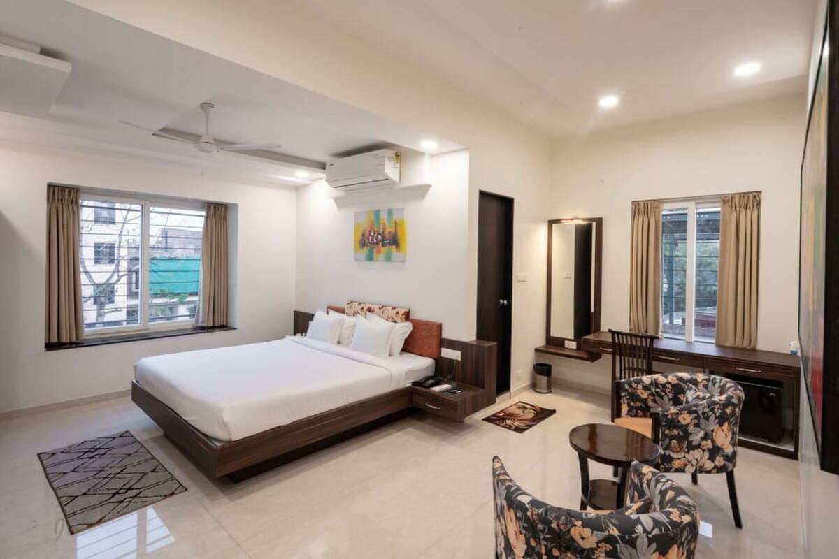 A hotel room with a large bed, a desk with a chair, a small table, and a mirror.