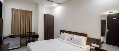 Een hotelkamer met een bed, bureau, stoel, kast en een spiegel.