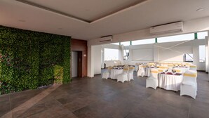 A spacious room with a green wall, white tables, and chairs, and large windows. - Springdale Suites - Nagpur (Nagpur)