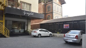 A building with a sign reading "Springdale" and a parking sign. Two cars are parked in front. - Springdale Suites - Nagpur (Nagpur)