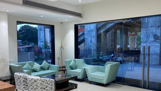 A modern living room with a large glass door leading to an outdoor area, a sofa, a coffee table, and a lamp. - Springdale Suites - Nagpur (Nagpur)
