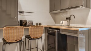A compact kitchen with a built-in dishwasher, a toaster, and wicker bar stools.