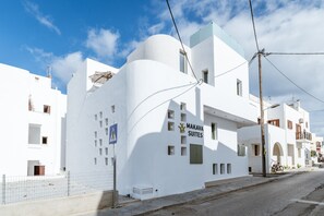 A white building with Makava Suites signage, a pedestrian crossing sign, and a bicycle parked outside. - Apartment In A Hotel 'Makava Family Suite' with Private Terrace, Wi-Fi and Air Conditioning (Naxos)