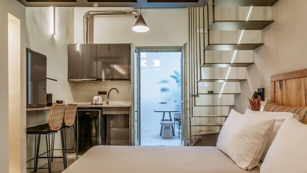 A modern hotel room with a bed, a kitchenette, a dining area, and a staircase.
