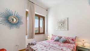 Un dormitorio con cama, mesita de noche, lámpara, ventana con cortinas y decoración en la pared.