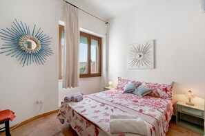 Une chambre à coucher comprenant un lit, une table de chevet, une lampe, une fenêtre avec des rideaux et des œuvres d’art murales.