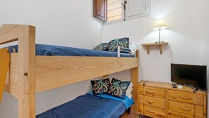 Una cama individual superpuesta con un televisor y un aparador de madera en una habitación con paredes blancas y una ventana.