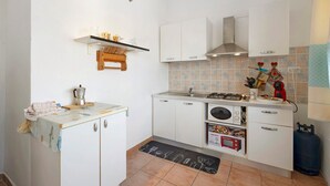 A compact kitchen with white cabinets, a gas stove, a microwave, and a small countertop. - Studio Apartment "Casa Silvia" with Sea View, Balcony & Air Conditioning (La Maddalena)