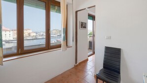 A room with a large window, a chair, and a view of a marina. - Studio Apartment "Casa Silvia" with Sea View, Balcony & Air Conditioning (La Maddalena)