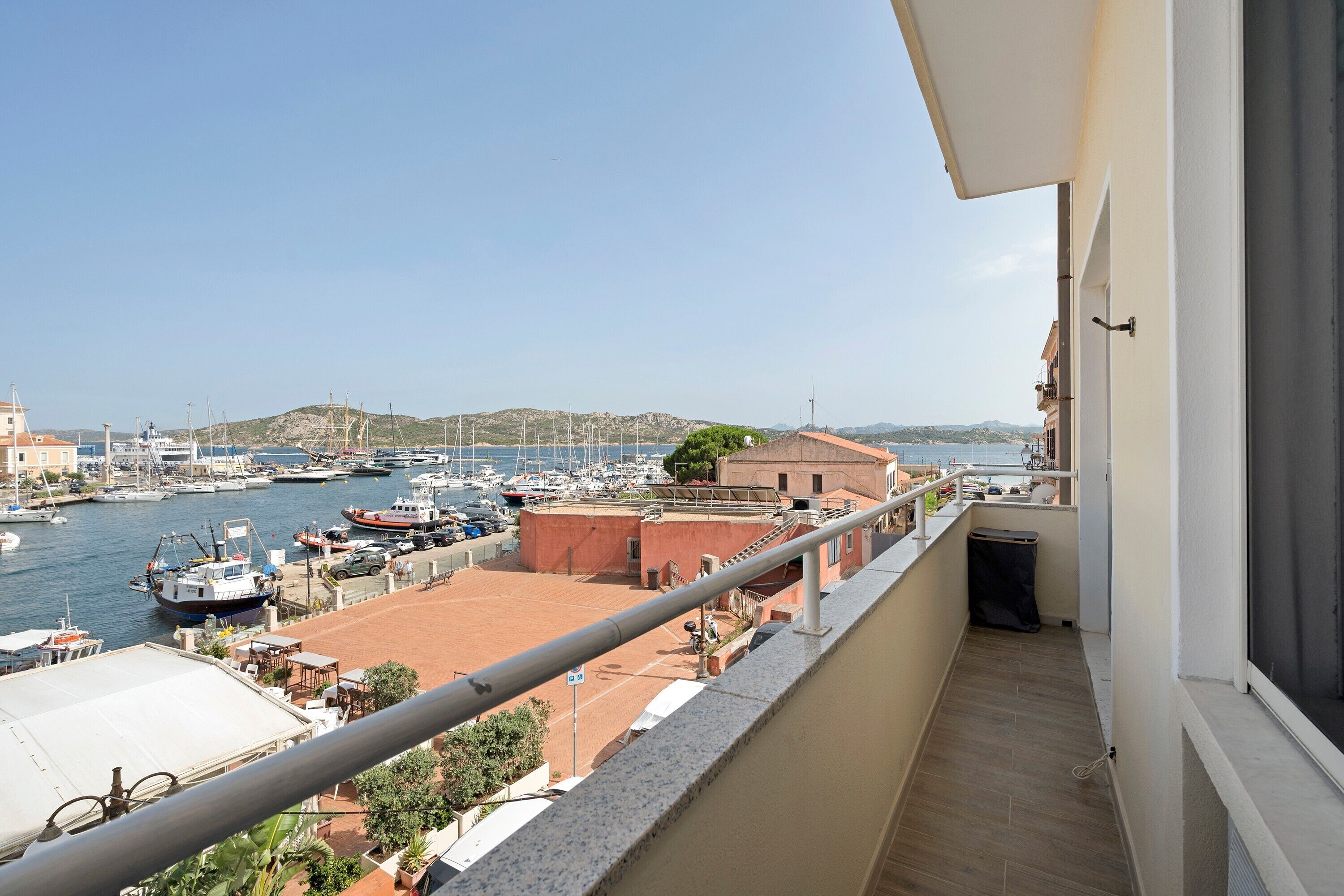 Un balcone con vista su un porto turistico, barche e colline in lontananza.