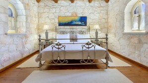 A stone-walled bedroom with a bed, two bedside lamps, and a painting on the wall.