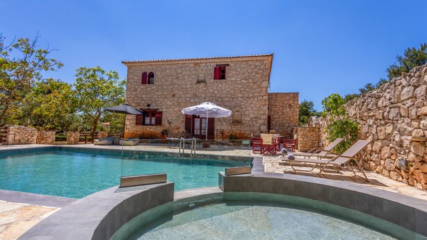 A stone building with a swimming pool, outdoor seating, and a stone wall.