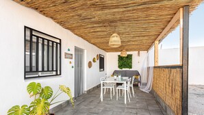 Un patio couvert avec une table et des chaises, un pot de fleurs et un espace barbecue.
