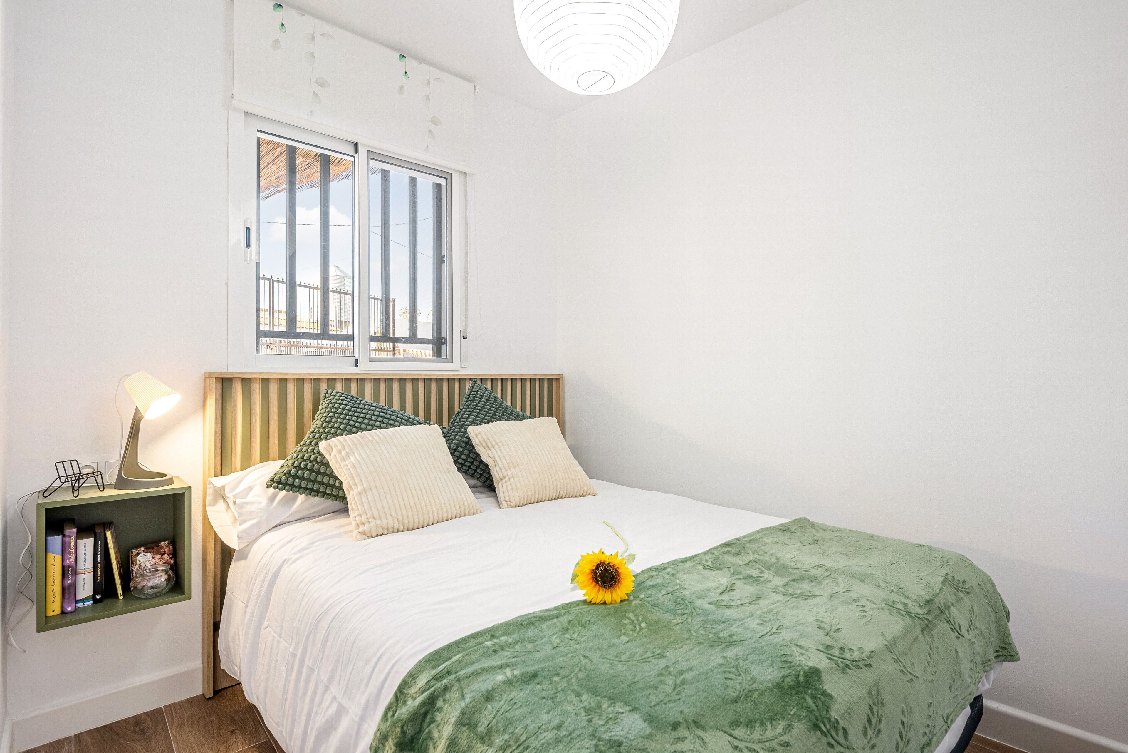 Ein Schlafzimmer mit einem Bett, einem Nachttisch, einem Fenster und einer grünen Decke.