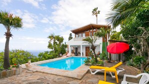 Un espace piscine avec une terrasse en pierre, des chaises longues et un bâtiment doté d’un balcon.