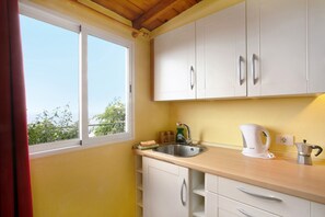 A kitchen with white cabinets, a sink, a kettle, and a window with a view of greenery. - Holiday Apartment "Welcome In Paradise" with Sea View, Shared Pool & Wi-Fi (La Matanza de Acentejo)