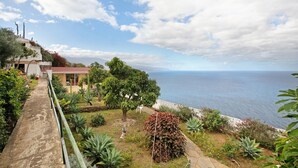 Une propriété située sur la côte, dotée d’un chemin pavé, d’un jardin avec différentes espèces de plantes et offrant une vue sur la mer.