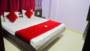 A bed with white and red bedding, a red throw blanket, and two red pillows. - Hotel Royal Palace (Ujjain)