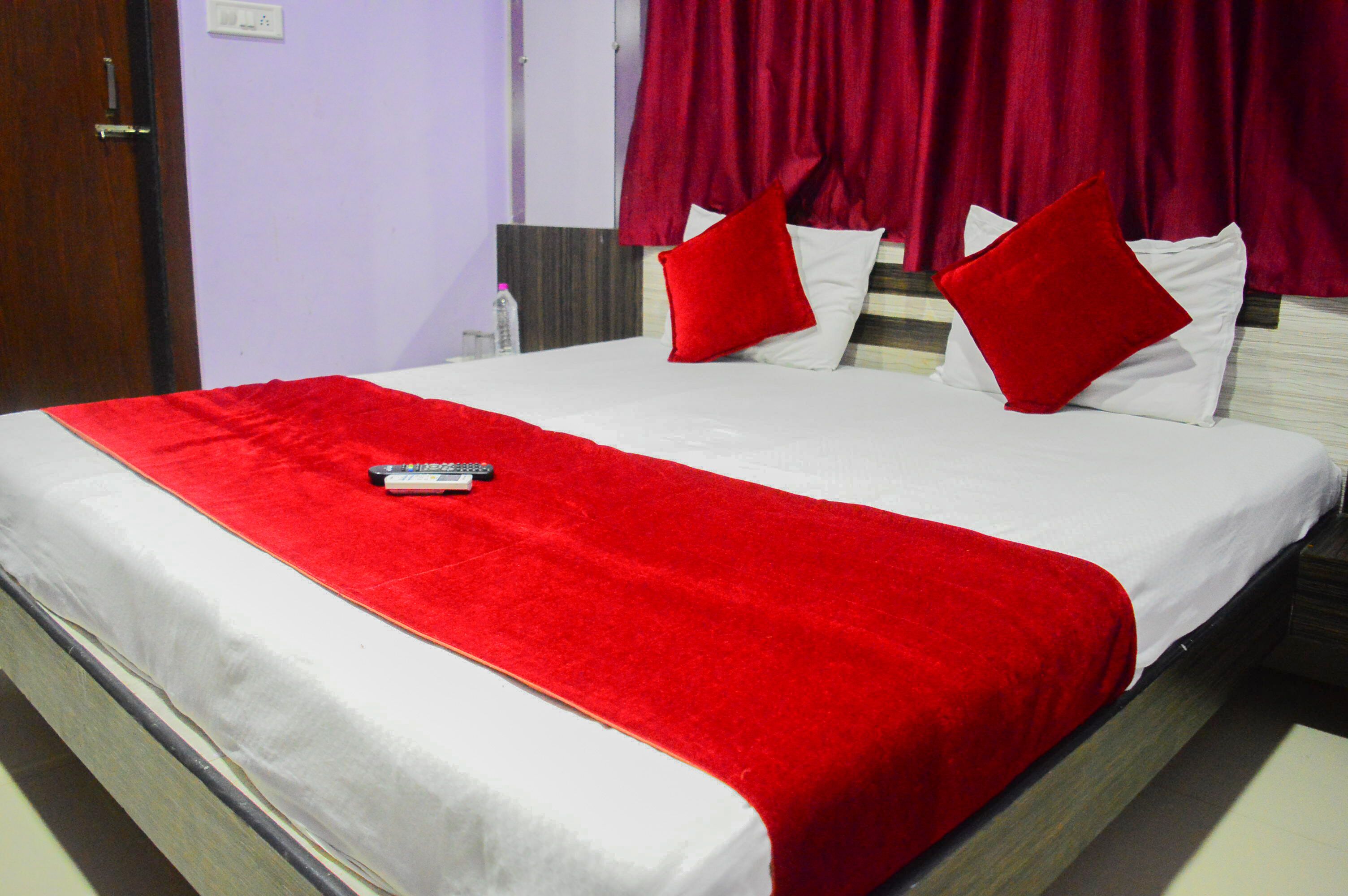 Habitación de hotel con cama, ropa de cama roja y blanca, y un control remoto sobre la cama.