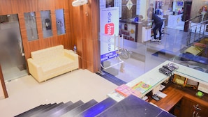 A hotel reception area with a sofa, a reception desk, and a glass partition. - Hotel Royal Palace (Ujjain)