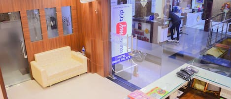 Zona de recepción de un hotel con un sofá, un mostrador de recepción y un panel de vidrio.