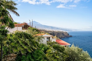 Une vue côtière avec une montagne, un bâtiment blanc doté d’un toit rouge et une végétation luxuriante.