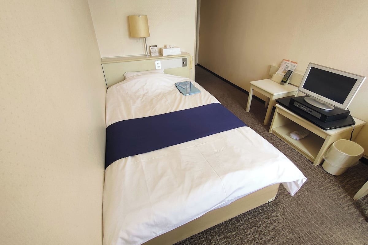 Habitación de hotel con cama, escritorio, computadora, monitor, lámpara y basurero.