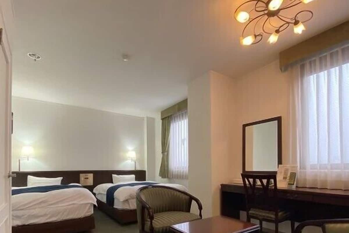 Habitación de hotel con dos camas, un escritorio, una silla y un espejo grande.