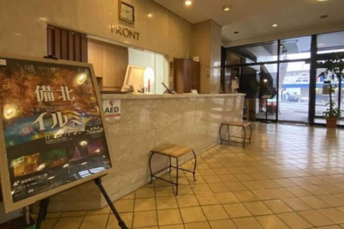 Zona de recepción de un hotel con suelo de baldosas, mostrador de recepción, un pequeño espacio de espera y un cartel en la pared.