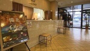 A hotel reception area with a tiled floor, a reception desk, a small seating area, and a poster on the wall.
