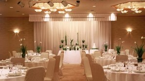 A banquet hall with round tables set for dining, chairs, and a stage with curtains in the background.