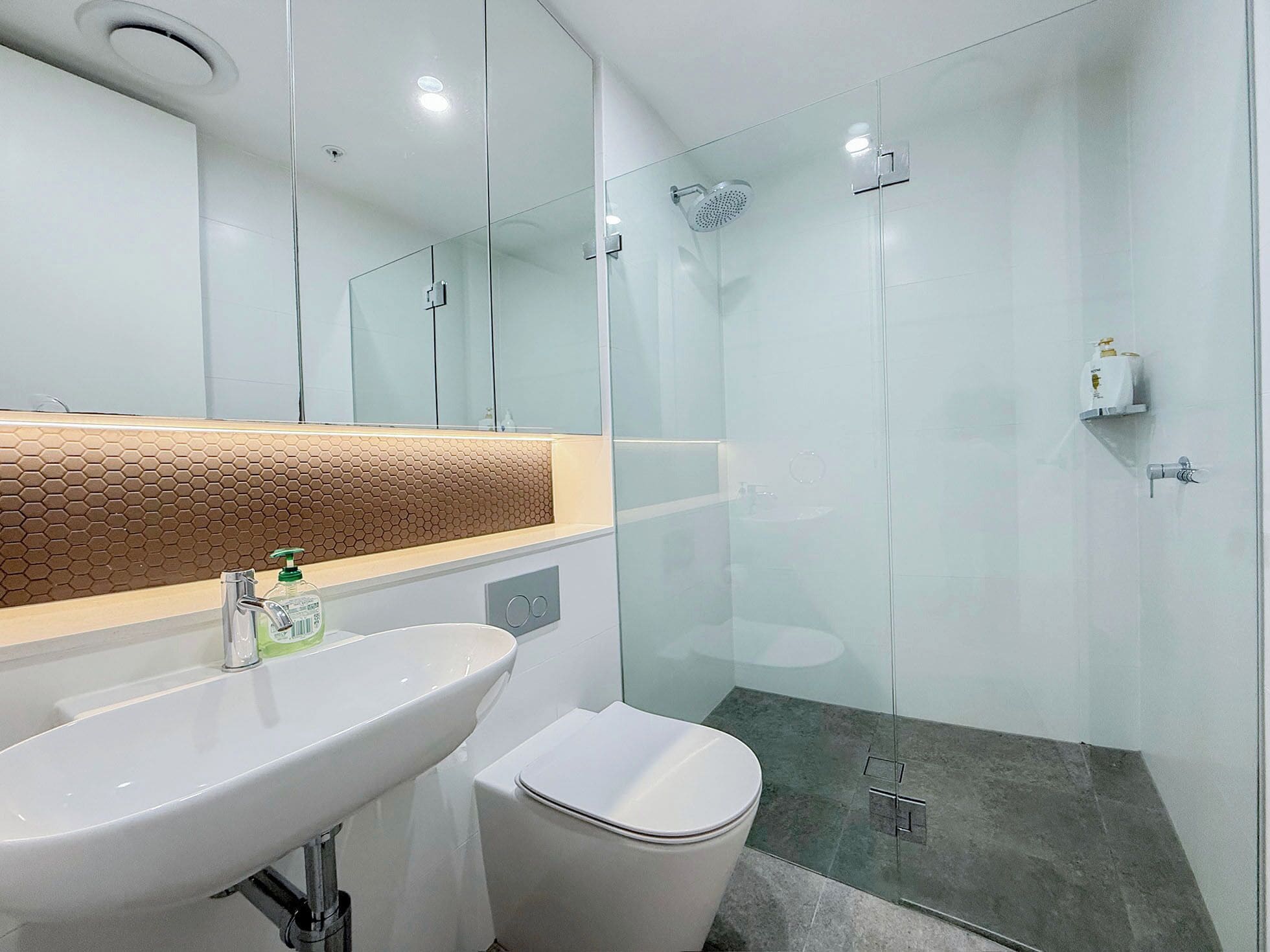 A modern bathroom with a glass shower enclosure, a white sink, and a toilet.