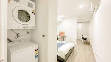 Ein Hotelzimmer mit Waschmaschine, einem Bett, einem Schreibtisch und einem Stuhl.