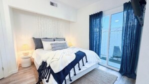 Een moderne slaapkamer met een bed, nachtkastje en een groot raam met gordijnen.