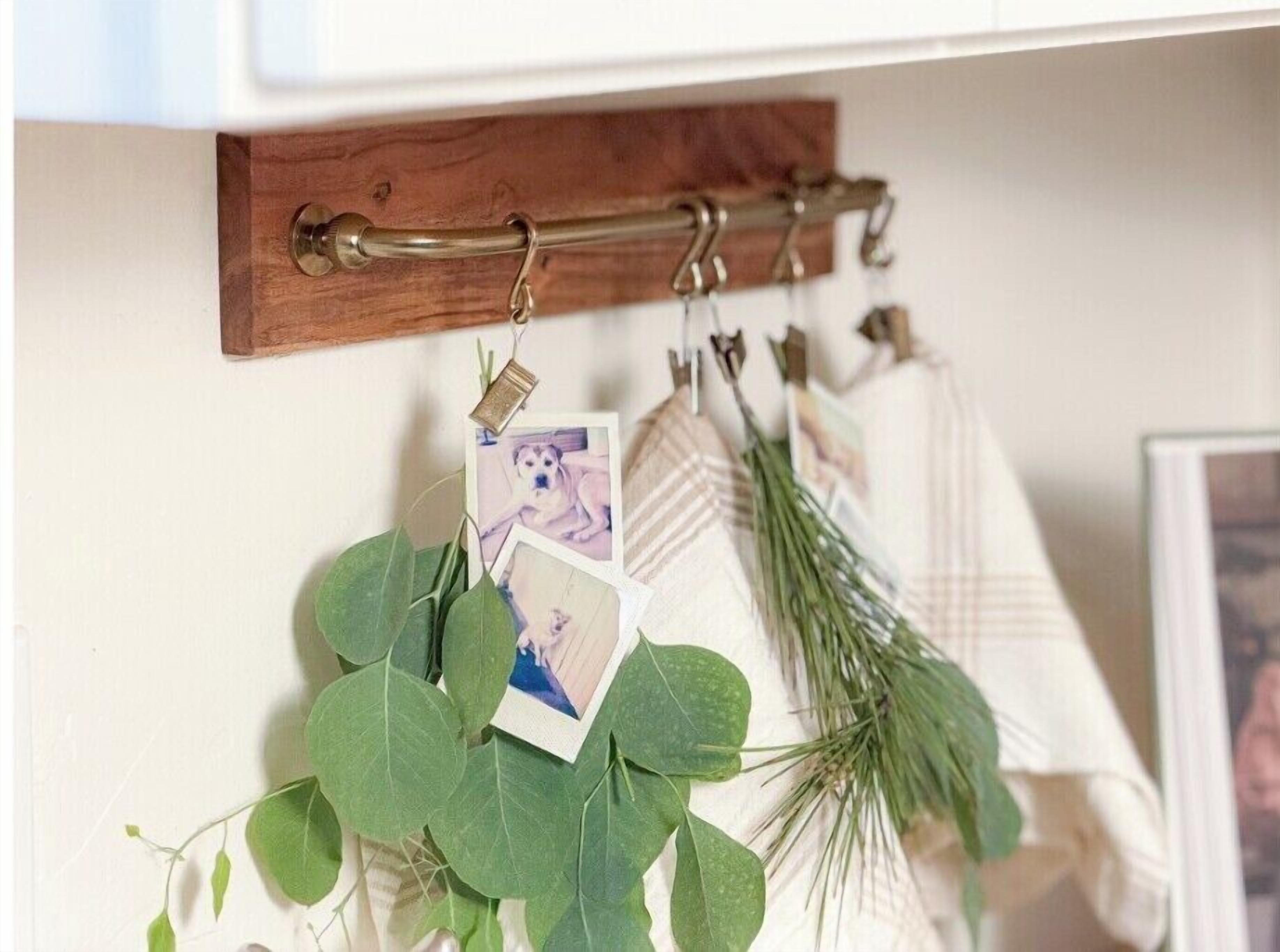 A wooden coat rack with a brass handle, holding several hangers and a few photographs.