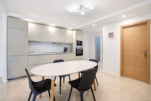 Une cuisine moderne avec des meubles blancs, une table de salle à manger ronde et des chaises noires.