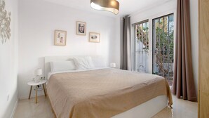 Un dormitorio moderno con una cama grande, una mesita de noche, una lámpara de pared y vistas al exterior a través de una puerta corredera.