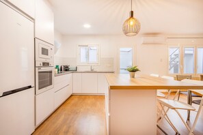 A modern kitchen with white cabinetry, a wooden countertop, and a hanging pendant light.