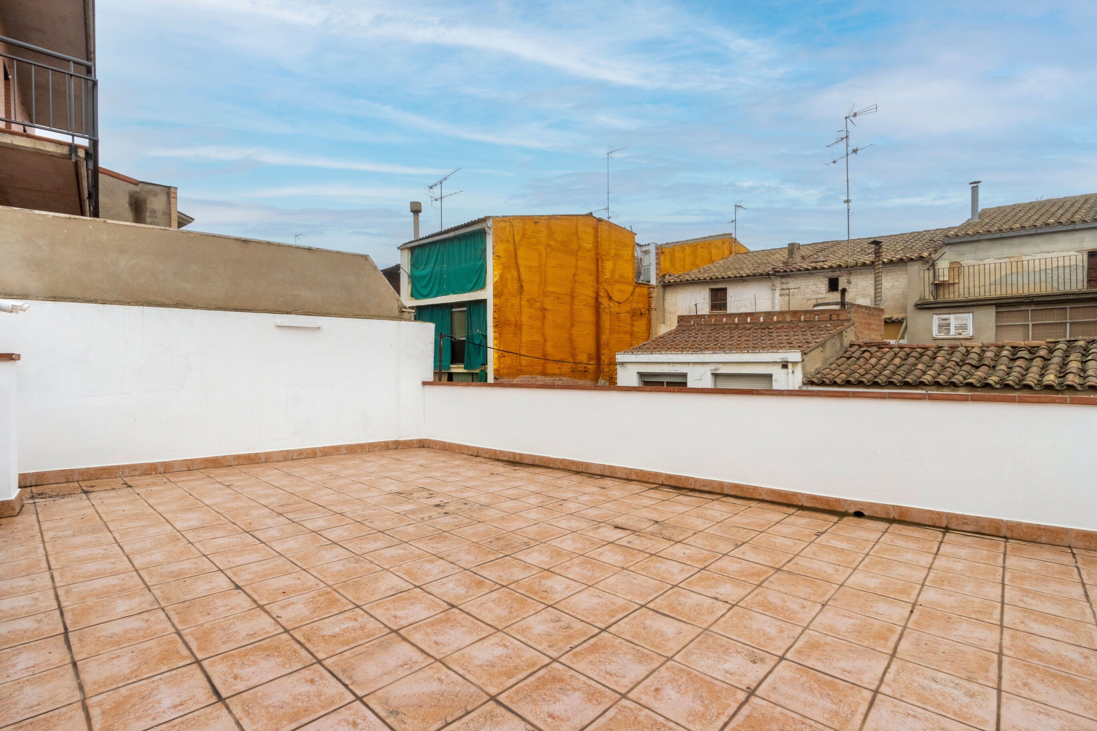 Terraza en la azotea con suelo de baldosas, rodeada de edificios con techos planos y antenas visibles.