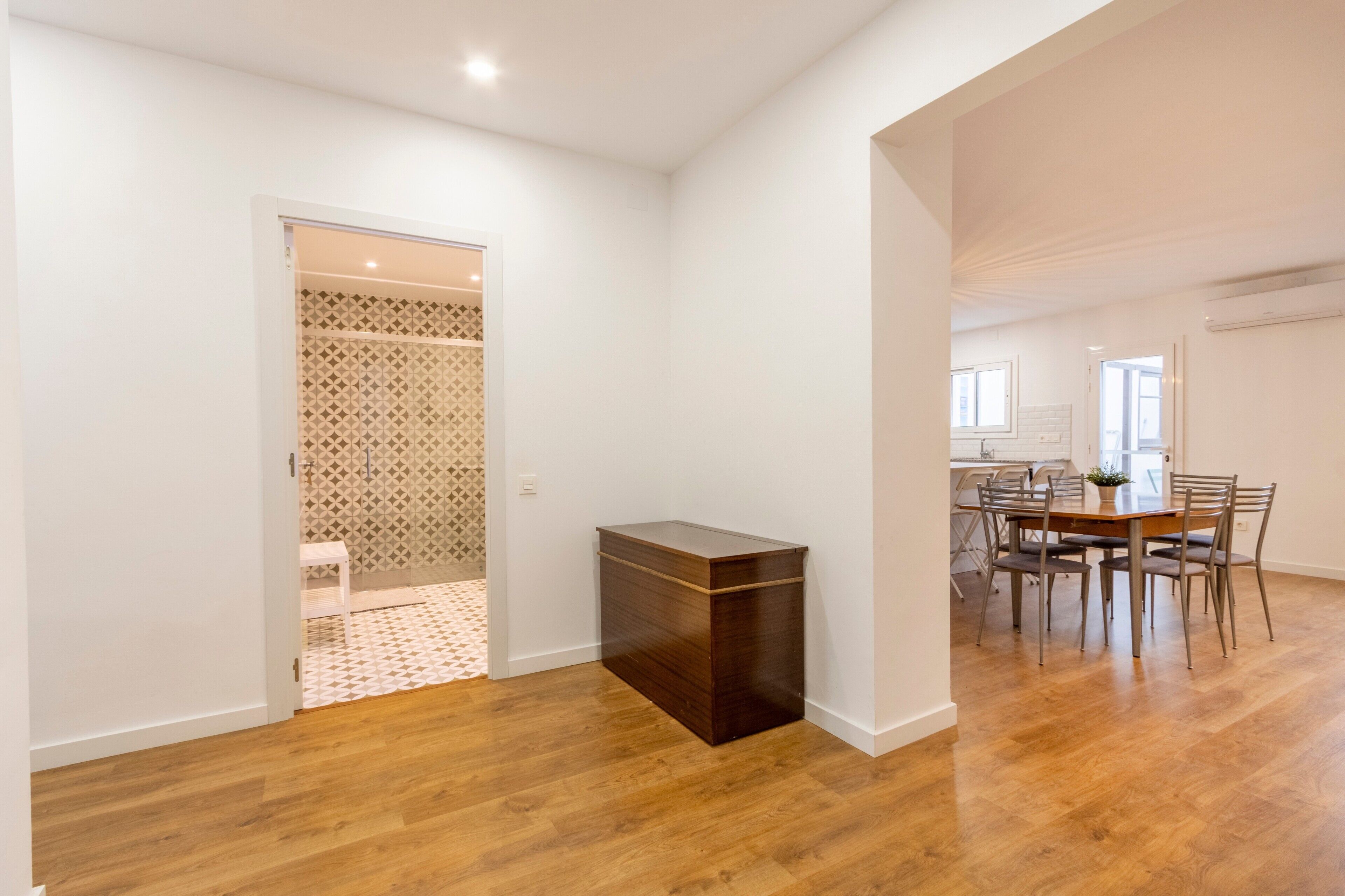 Une pièce avec un plancher en bois, un coin repas comprenant des chaises et une table, et un petit meuble.